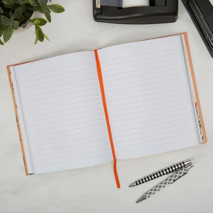 Open notebook with lined pages on a desk with a pen and plant