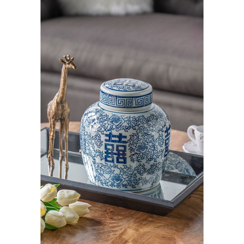 Blue and white ceramic jar with floral patterns on a wooden table with other decorative items