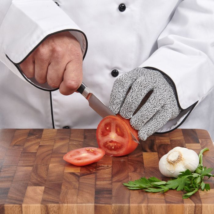Chef wearing a cut-resistant glove and cutting tomatoes on a wooden board.