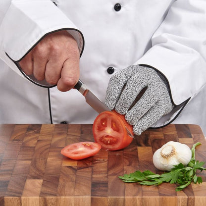 Chef wearing a cut-resistant glove and cutting tomatoes on a wooden board.