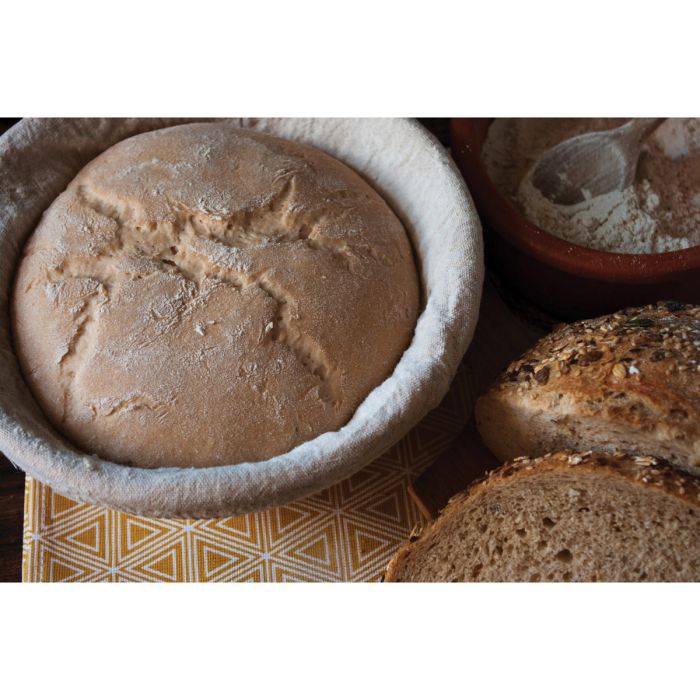 Loaf of bread in a proofing basket with additional loaves on a patterned surface