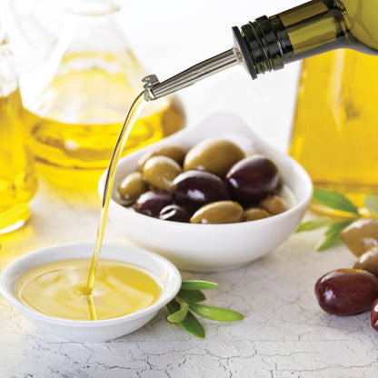 Olive oil being poured into a bowl with olives on a light surface