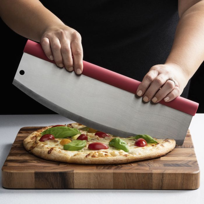 Person using a pizza cutter to slice a pizza topped with tomato and basil on a wooden board