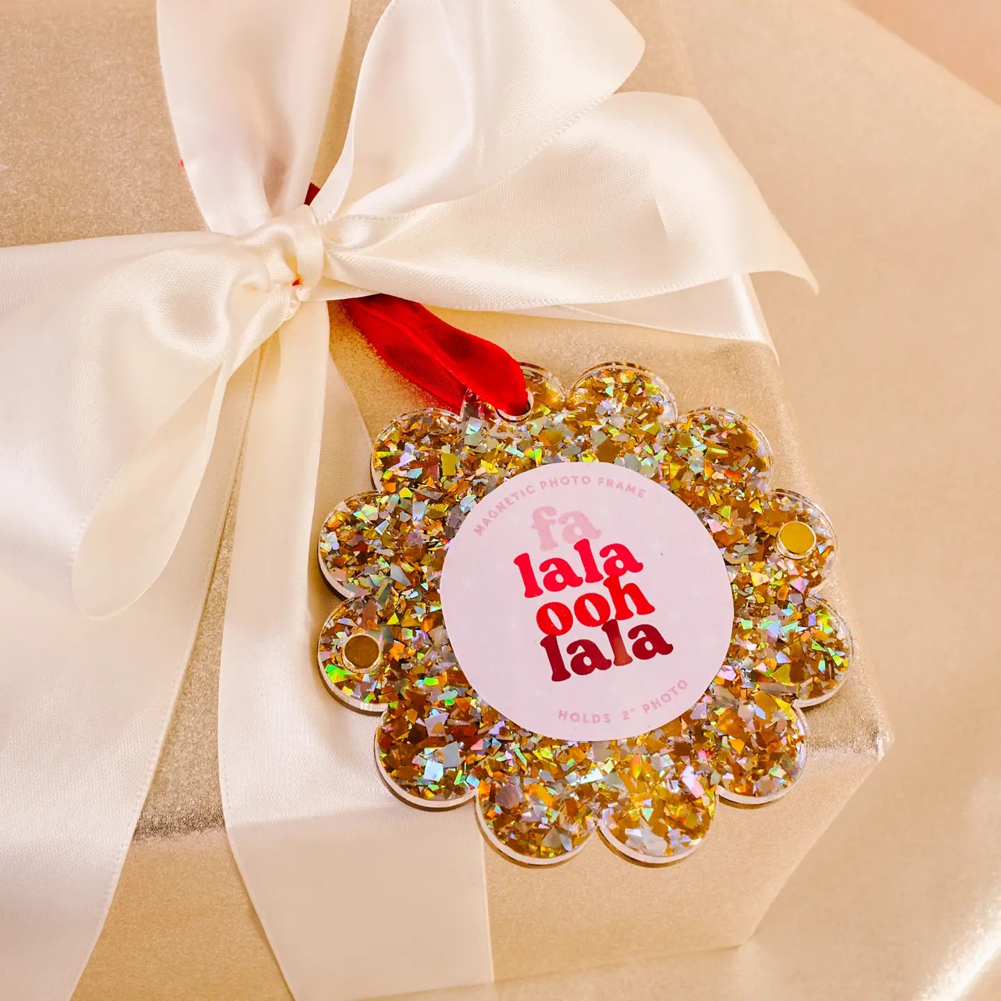 gold glitter Scalloped Acrylic Frame Ornament tied in an ivory bow of a wrapped gift