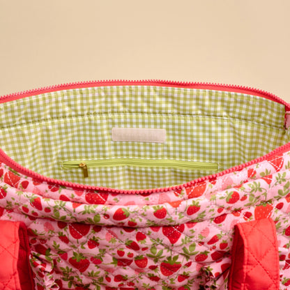 Close-up of a fabric bag with strawberry pattern and green checkered interior.