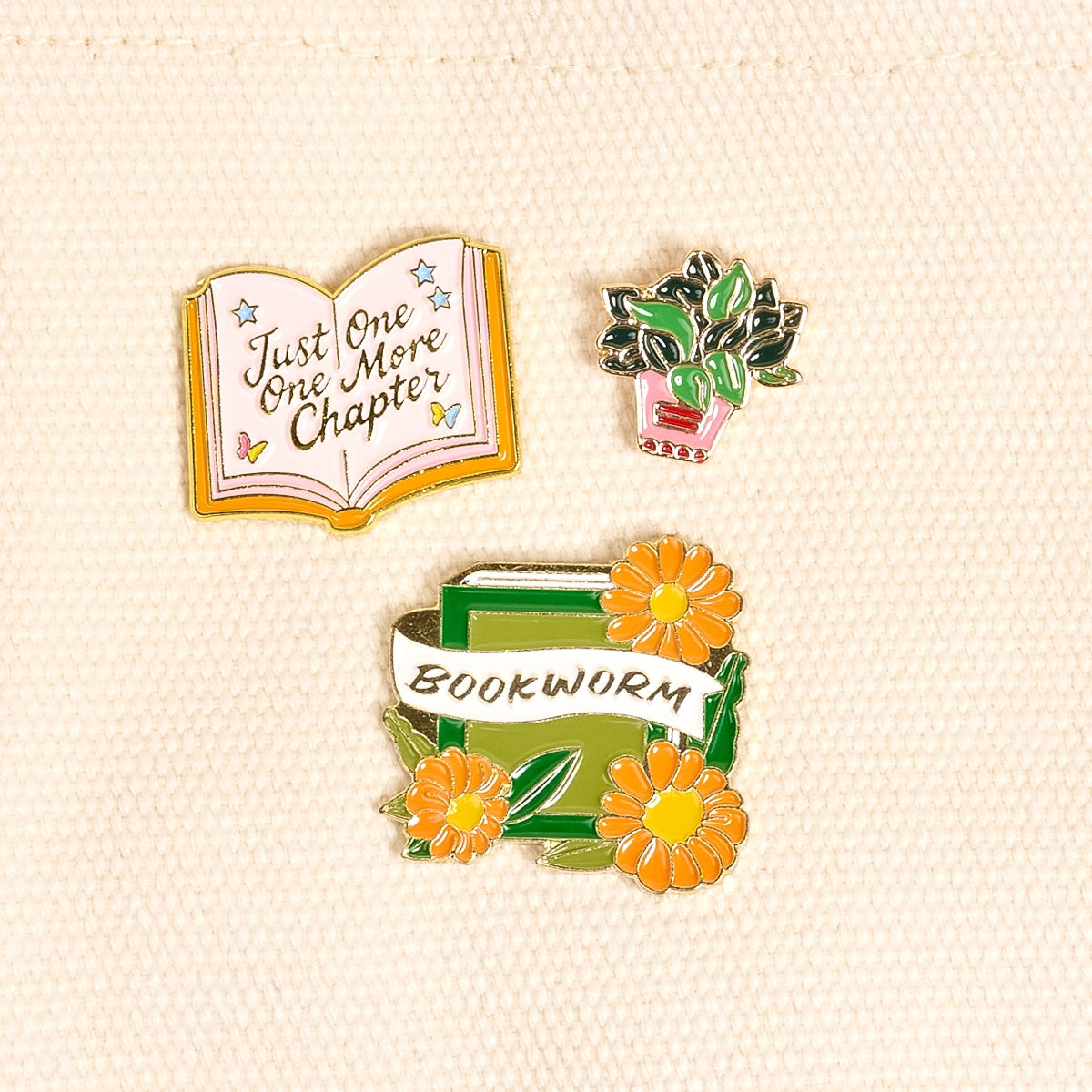Three pins featuring book-themed designs on a beige background