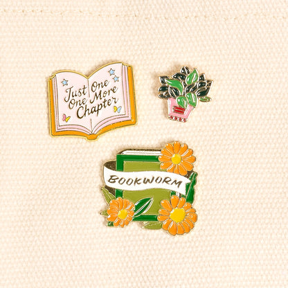 Three pins featuring book-themed designs on a beige background