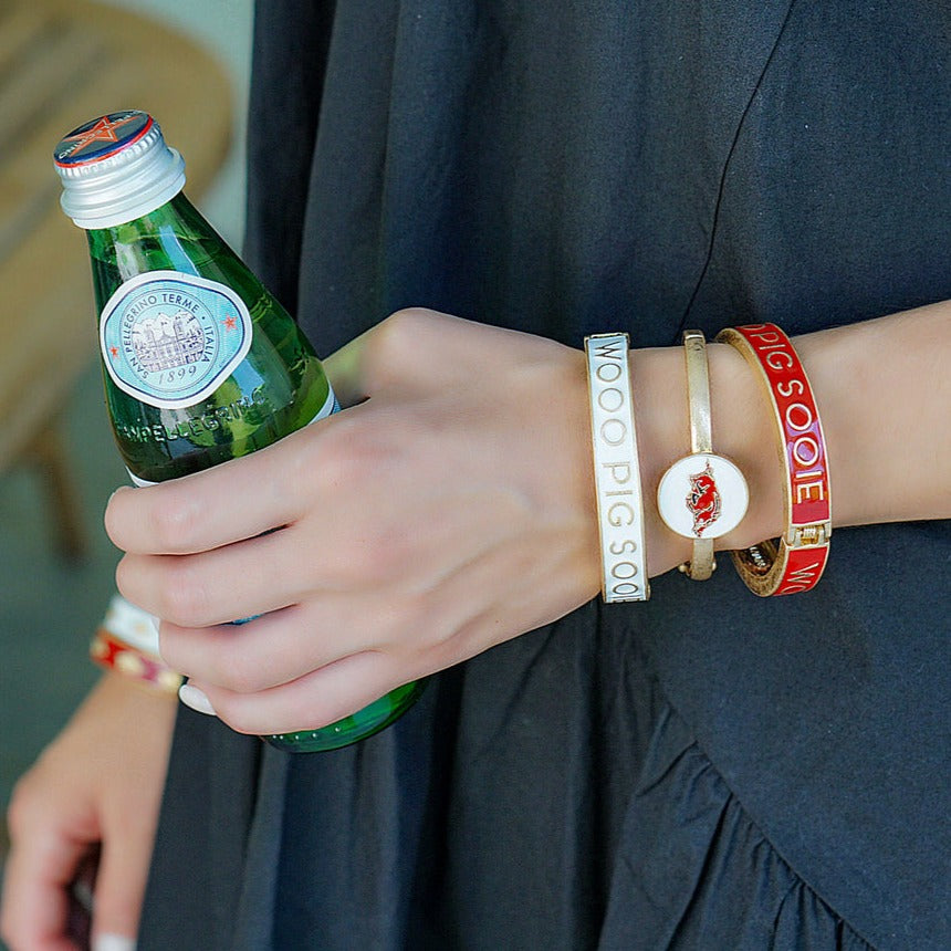 person holding a green glass bottle and all 3 razorback bangles on their arm.