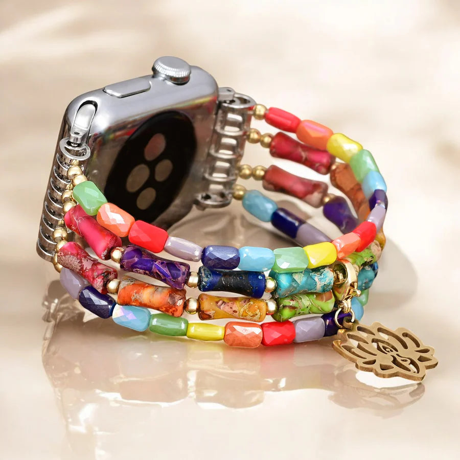 Colorful beaded watch strap with gold lotus charm on a neutral background