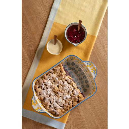 Baked dessert in a decorative dish with a side of jam on a wooden table.
