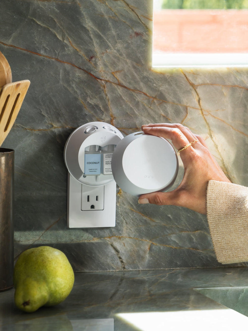 hand putting the cover on a Pura Device 4 that is plugged into an outlet above a kitchen countertop.