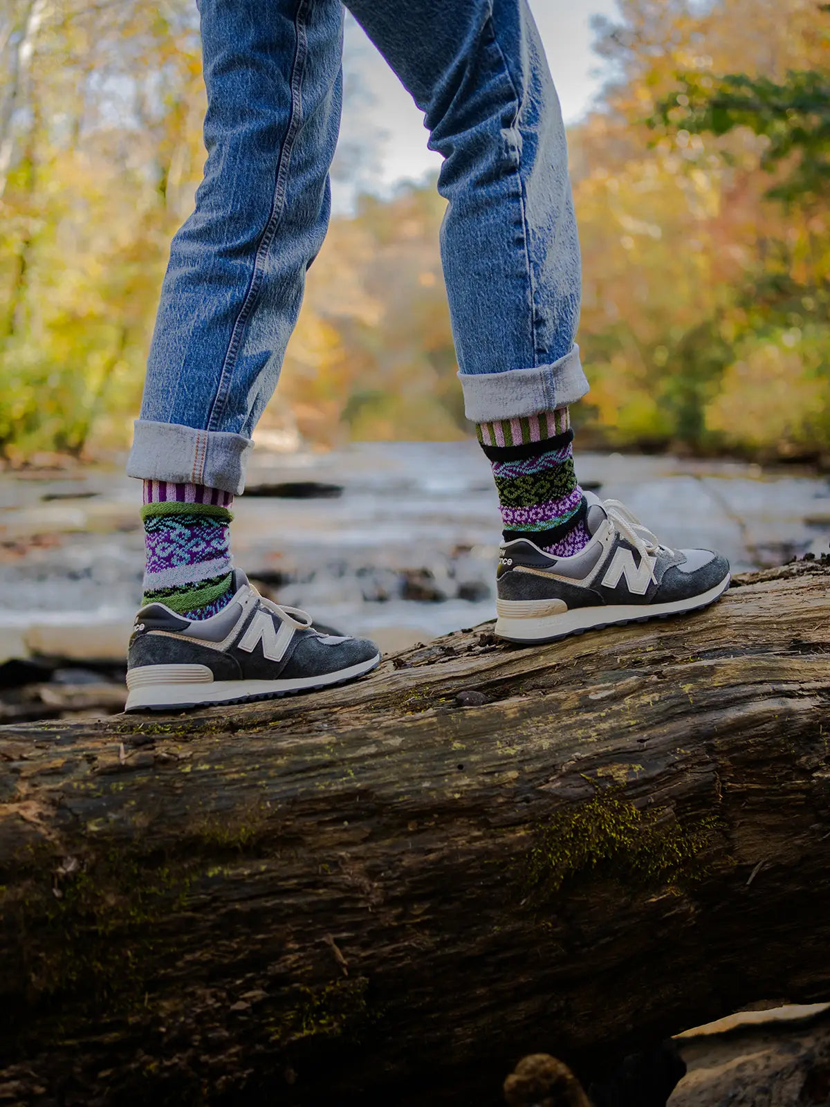 person wearing jeans, tennis shoes and La Seine Crew Socks walking across a log laying across a river