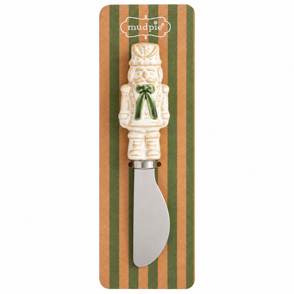 A ceramic nutcracker-shaped spreader knife with a silver metal blade, presented on a striped brown and green backing card 
