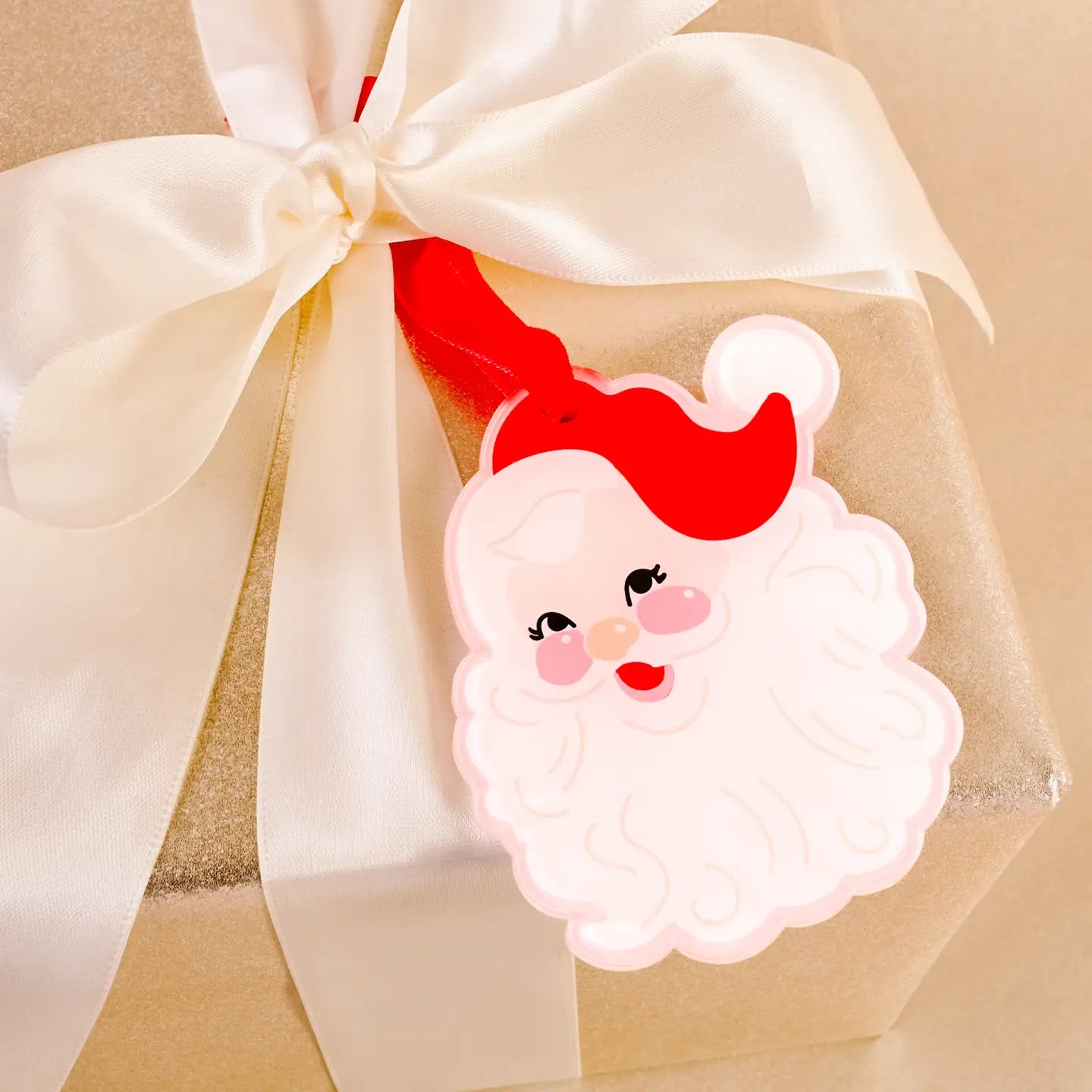 acrylic santa face ornament tie in the bow of a present wrapped in gold paper