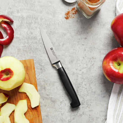 paring knife with black handle laying on a countertop surrounded by sliced apples and a jar of cinnamon.