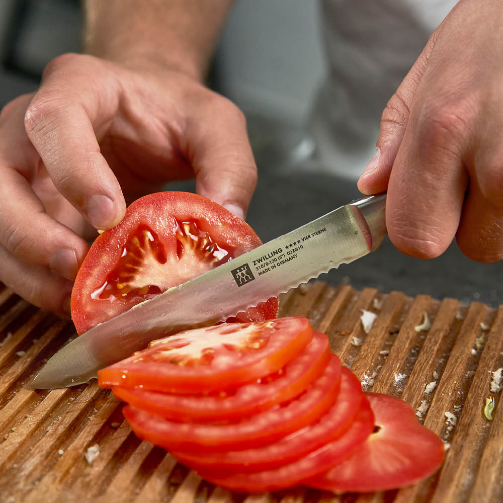 hand holding a Four Star 5 Inch Serrated Utility Knife and slicing a tomato.