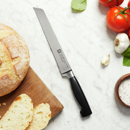 Four Star 8 Inch Bread Knife laying on a countertop with sliced bread, tomatoes, and herbs.