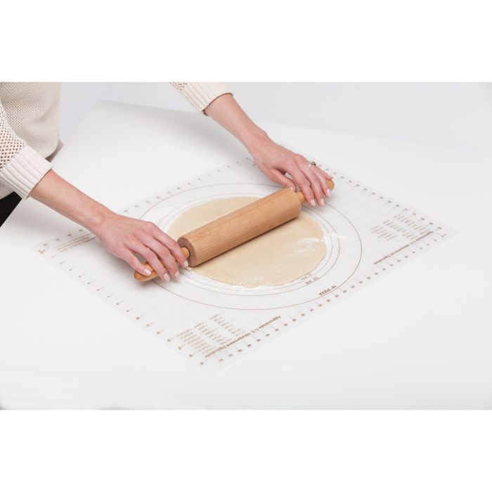Person rolling out dough with a wooden rolling pin on a pastry mat