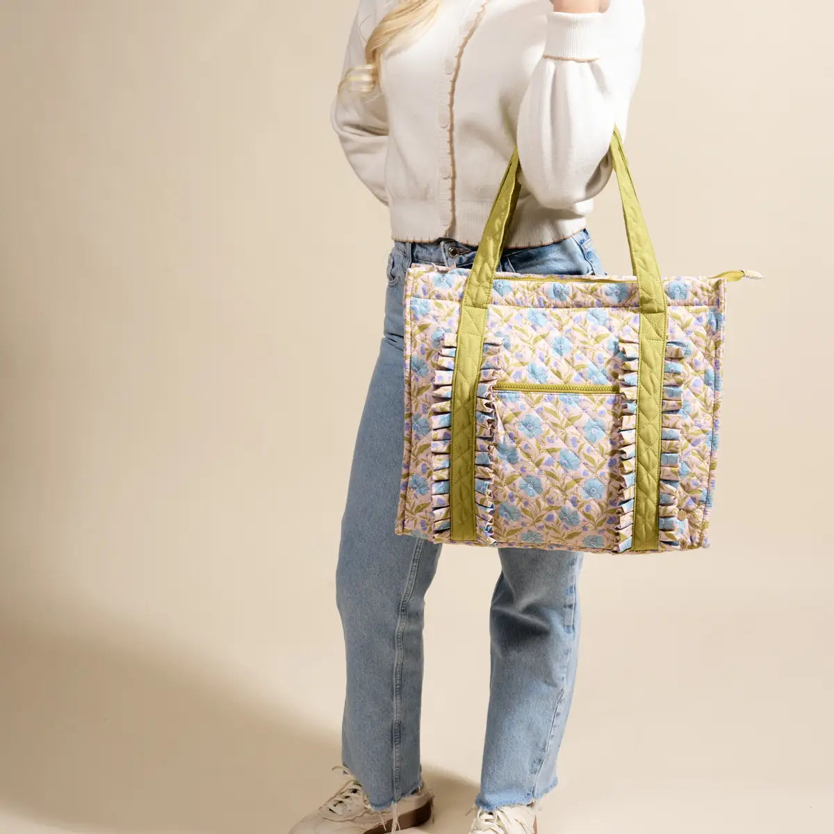 Person holding a aqua floral patterned tote bag with green straps against a beige background