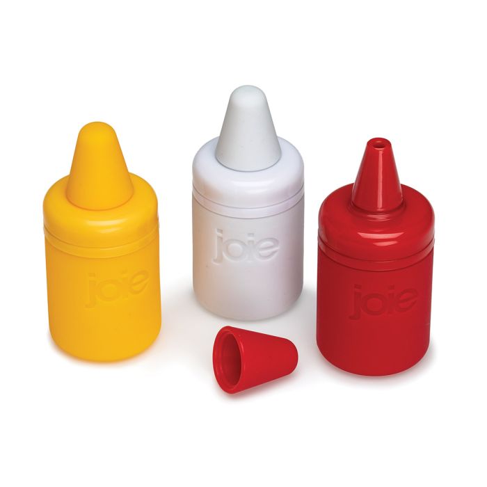 Three silicone squeeze bottles in yellow, white, and red, with the word 'joie' embossed on each, shown on a clean white background. A small detached red cap lies in front.