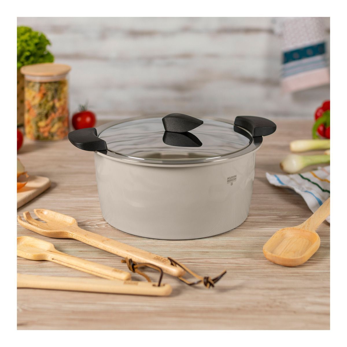 Hot pan set on a table with the lid on it and wooden spoons arranged around it.