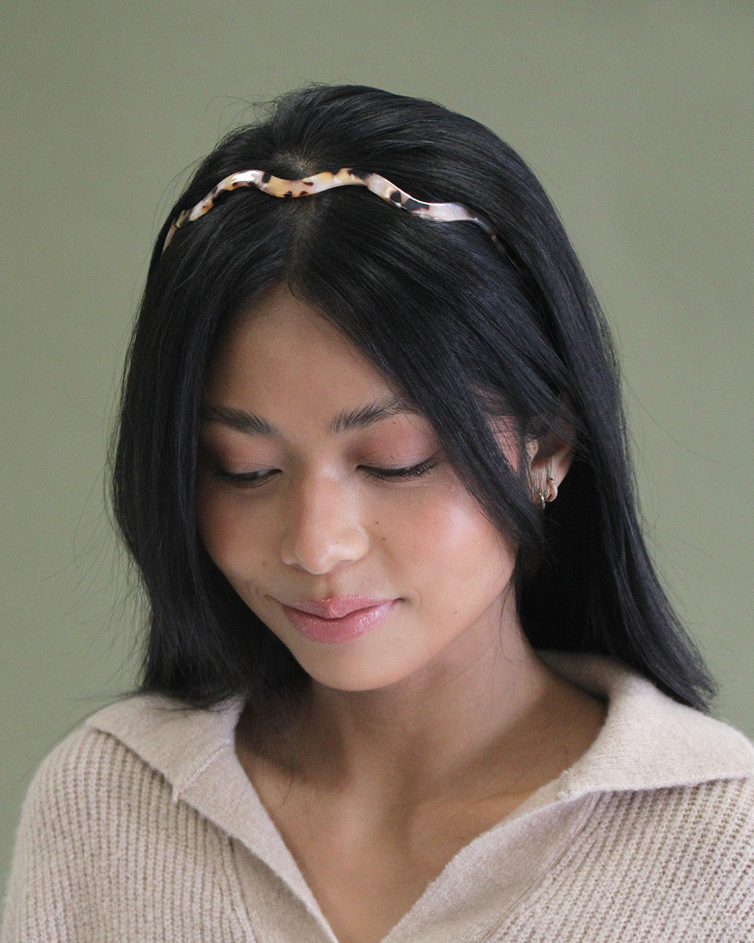person with black hair wearing a blush tortoise headband.