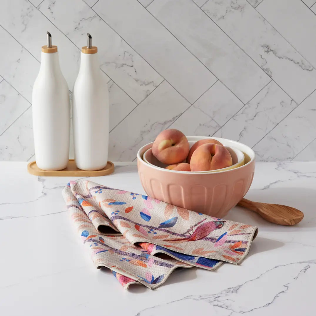 Birdsong towel with bird side showing draped on a counter next to a bowl full of Peaches.