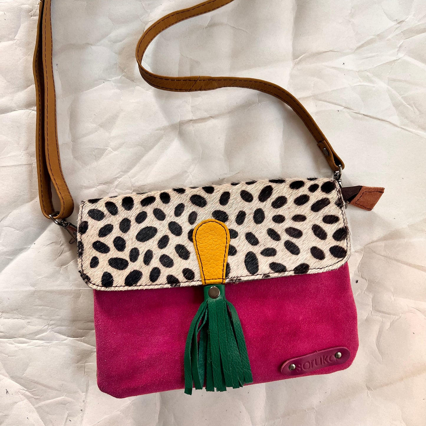 juliette bag with animal print flap, green tassel, and crossbody strap clipped on it.