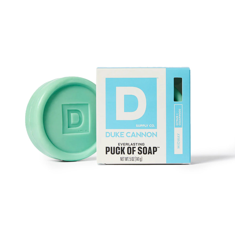 Mint green puck of soap next to its Duke Cannon packaging on a white background
