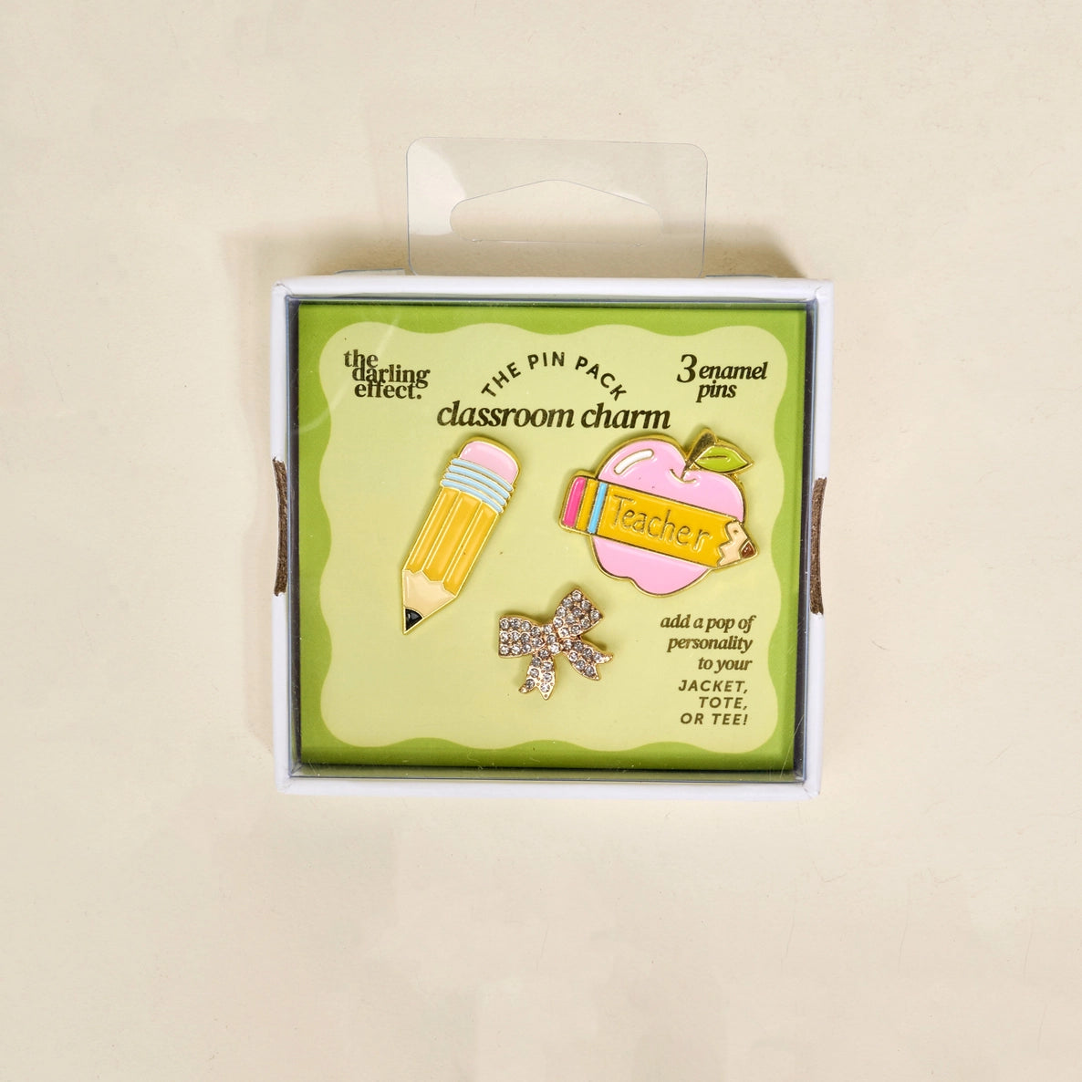 Set of three teacher themed enamel pins in a packaging box on a beige background