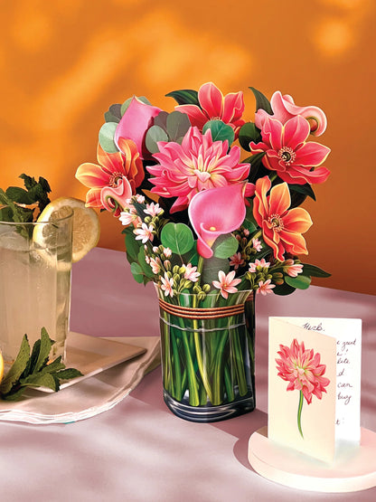 dear dahlia paper bouquet set on a table with a glass of lemonade and the enclosure card.