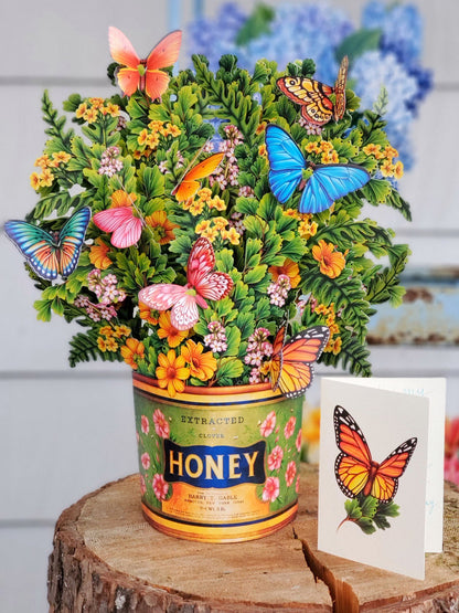 Butterflies & Buttercups flower bouquet set on a slab of wood with enclosure card that has a butterfly printed on it.