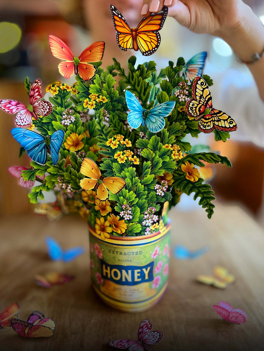 Butterflies & Buttercups paper flower bouquet set on a wooden table with paper butterflies scattered about.