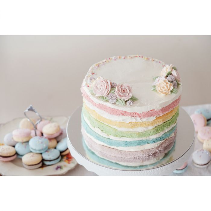 pastel rainbow cake with icing roses on top and cookie in the background