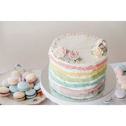 pastel rainbow cake with icing roses on top and cookie in the background