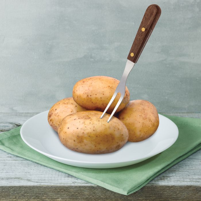 Four potatoes on a white plate with a granny fork in one of the potatoes on a green napkin and gray background