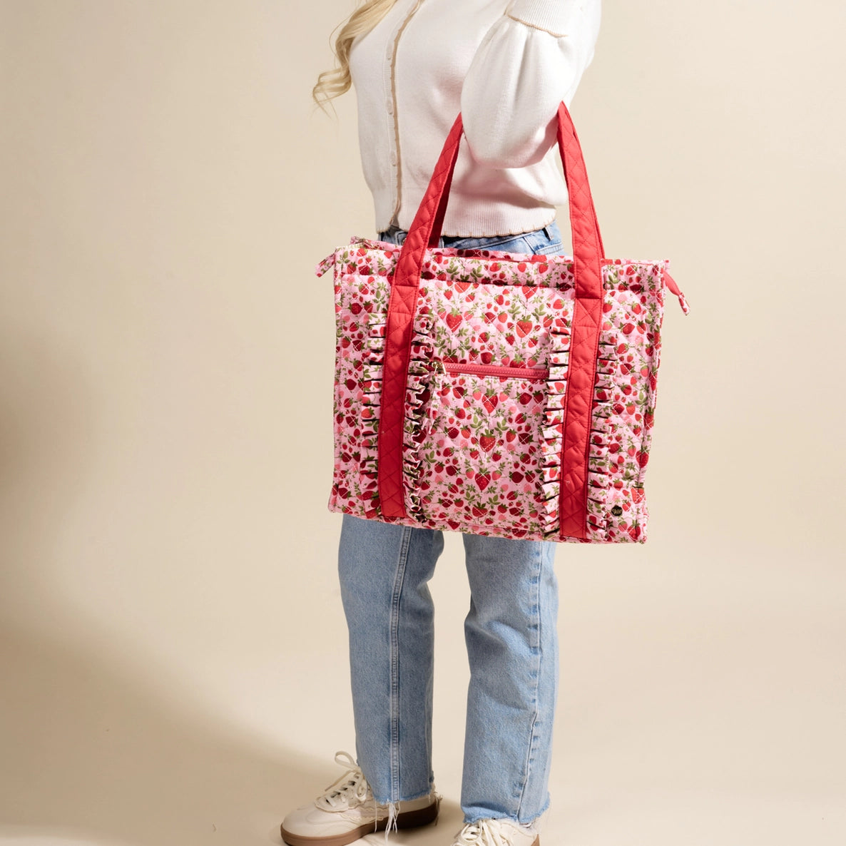 Person holding a strawberry-patterned tote bag with red straps against a beige background