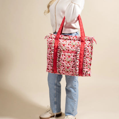 Person holding a strawberry-patterned tote bag with red straps against a beige background