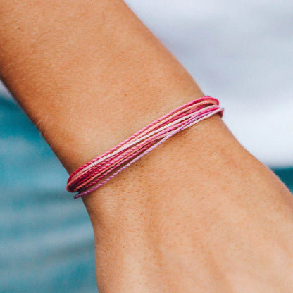 Pura Vida multi strand corded bracelet in varying shades of pink with a Pura Vida logo charm