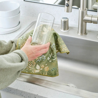 Hand using green botanical towel to clean a glass over the sink.