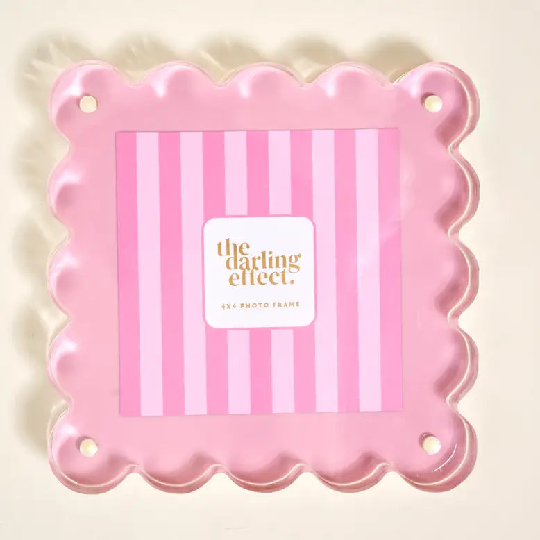 A pink scalloped photo frame with a striped insert on a light cream background.