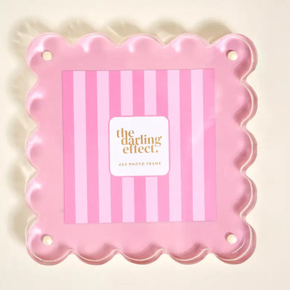 A pink scalloped photo frame with a striped insert on a light cream background.