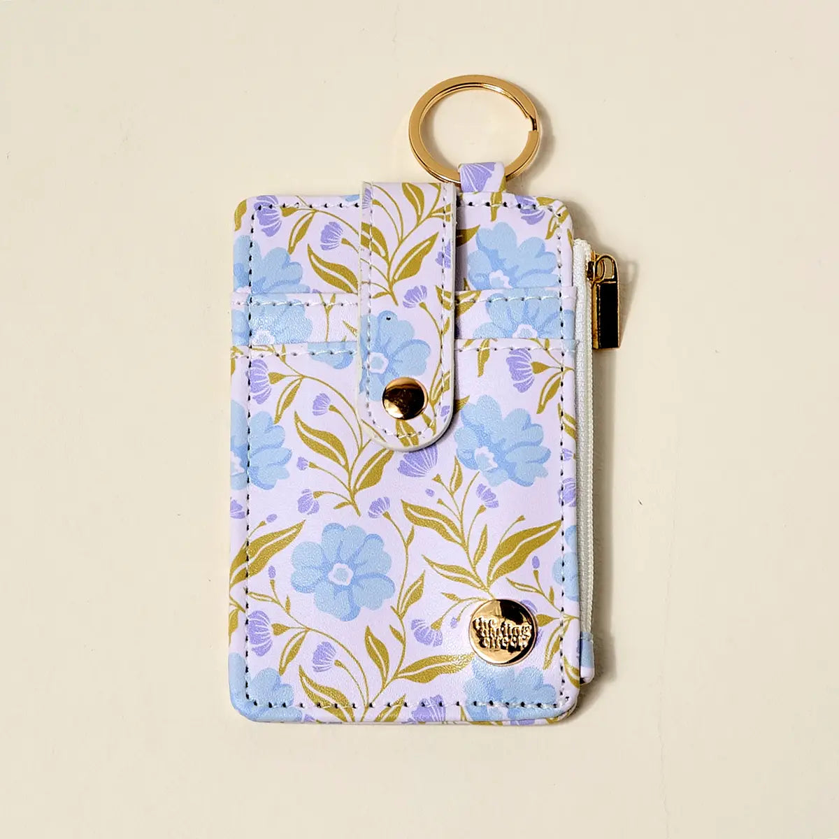 small wallet with blue and lavender floral design and gold key ring shown on a beige background