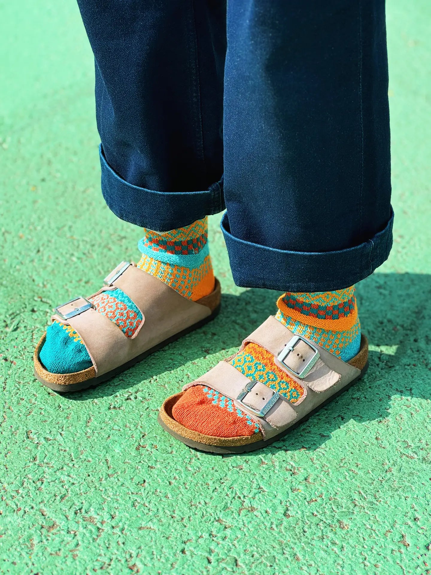 person wearing jeans, Birkenstocks and Dune Crew Socks standing on a green surface