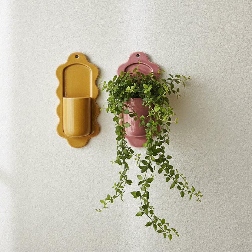 Two wall-mounted planters with a hanging green plant on an off-white wall.