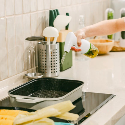 Person spraying oil into a black grill pan on a kitchen counter.