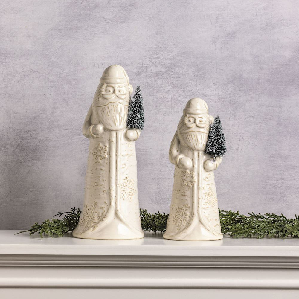 2 sizes of ceramic Santa figurines set on a mantle with greenery