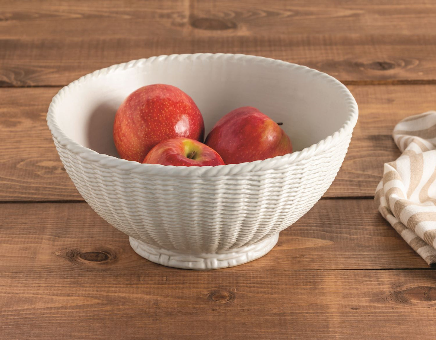 White woven bowl with red apples in it on a wooden surface