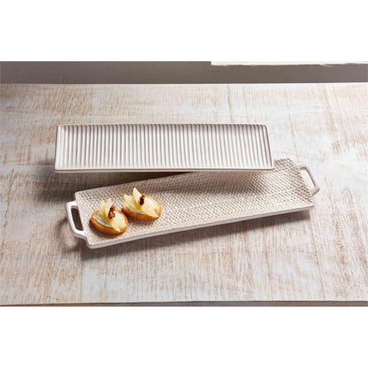 small tray with ribbed lines and large tray with handles and woven pattern arranged on a wooden table with snacks on the larger tray.