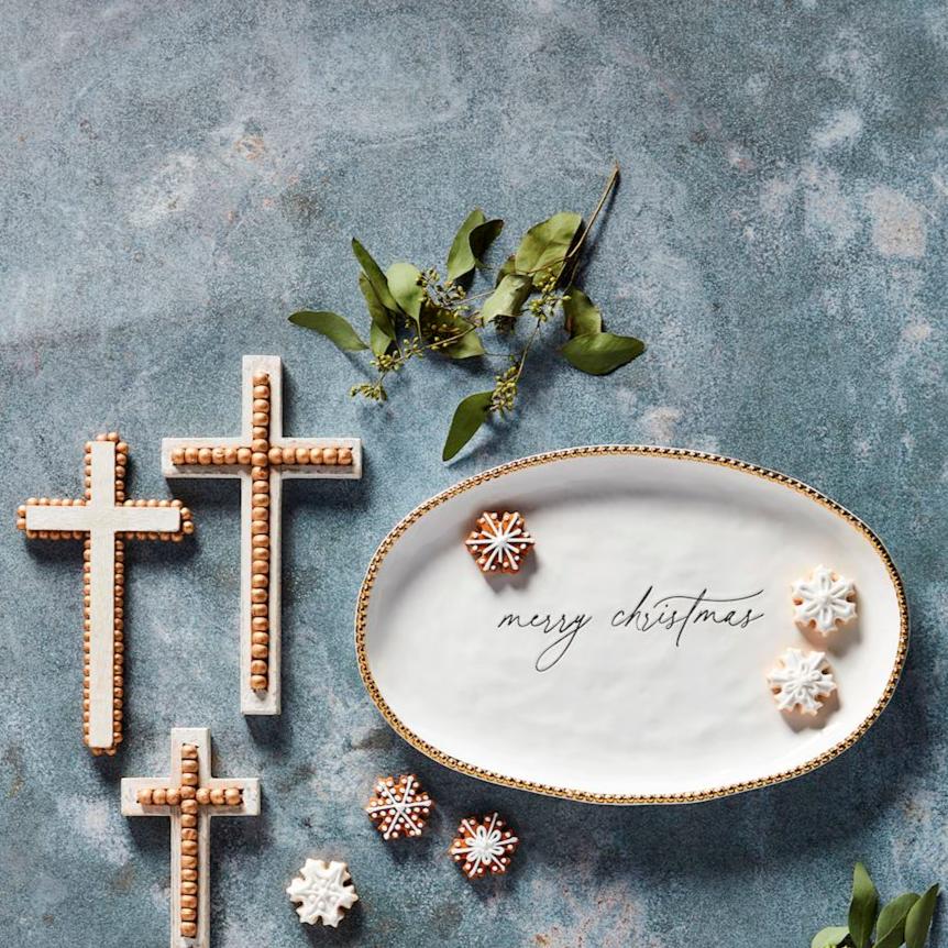 top view of a table arranged with the "merry christmas" platter with cookies on it and crosses and sprigs of greenery around it.